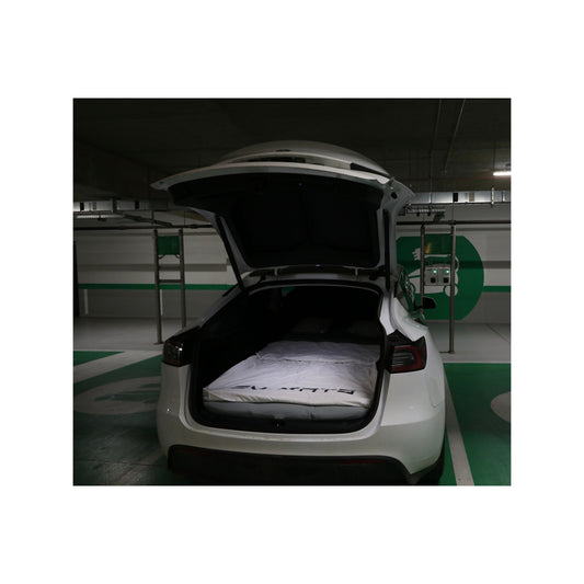 White Tesla Model Y parked in an underground car park, tailgate open, with the EV-MATS mattress made up as a bed in the boot under a white EV-MATS duvet.