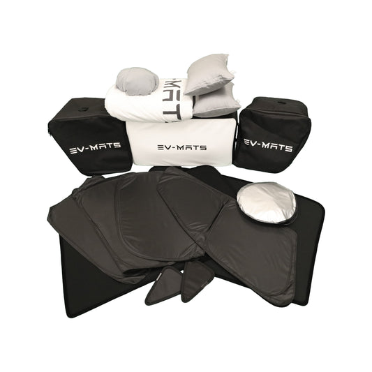 The EV-MATS Deluxe Camp Set on a white background: the folded white mattress between two black EV-MATS carrying bags, grey pillows and a white duvet on top, and the black privacy sun shade panels laid out in front.